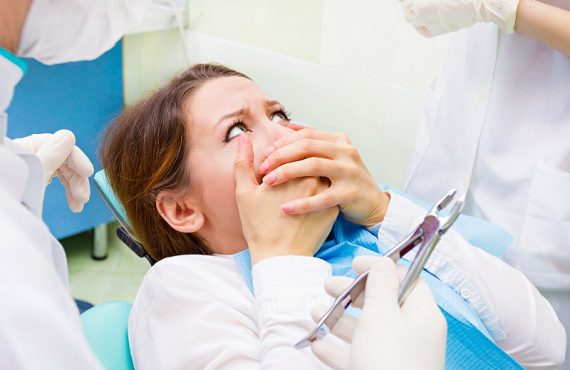 Egy fiatal nő ül a fogorvosi székben és fogja a száját, fél a fogorvosi vizsgálattól.