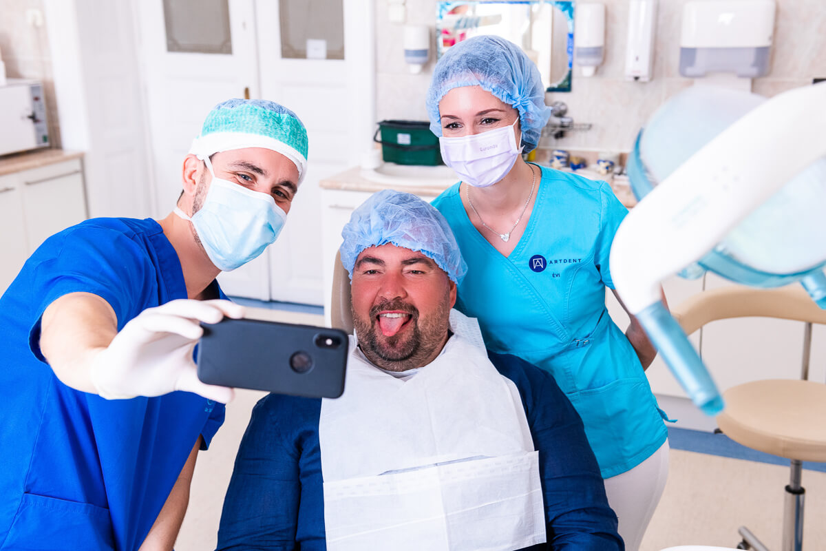 Dr. Varajti Artúr és kollégája az Artdent fogászat rendelőjében egy vidám, nyelvét öltő páciens mellett fotózkodnak