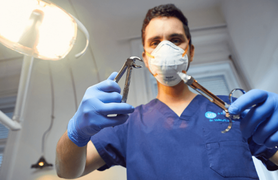 A képen Dr. Varajti Artúr fogorvos, szájsebész egy fogóval és egy érzéstelenítővel. A kép a fogszuvasodás megelőzésére hívja fel a figyelmet.