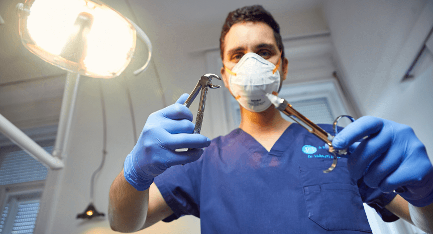 A képen Dr. Varajti Artúr fogorvos, szájsebész egy fogóval és egy érzéstelenítővel. A kép a fogszuvasodás megelőzésére hívja fel a figyelmet.